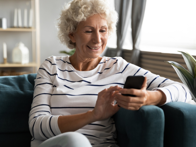 A middle-ages woman smiling at the FinalFYI message she received on her phone